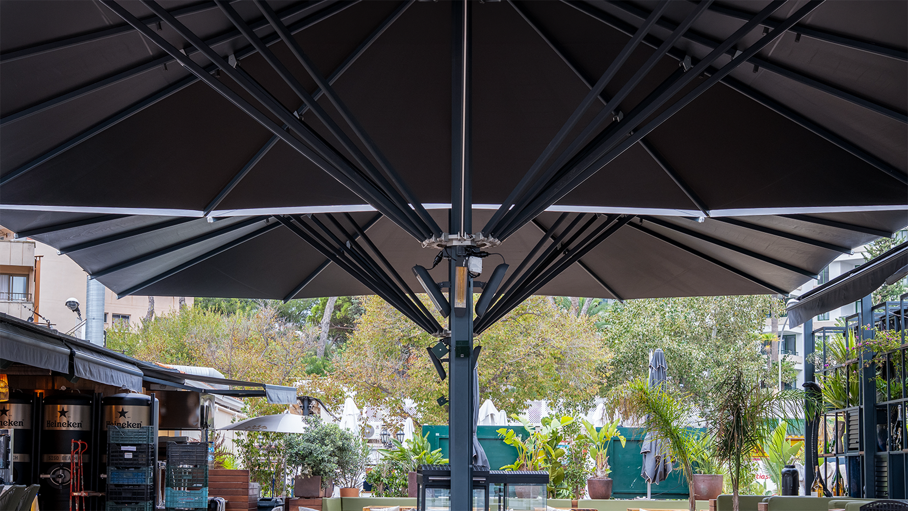 Terraza de restaurante vacía con mesas de madera, sillas tejidas y sombrilla grande negra