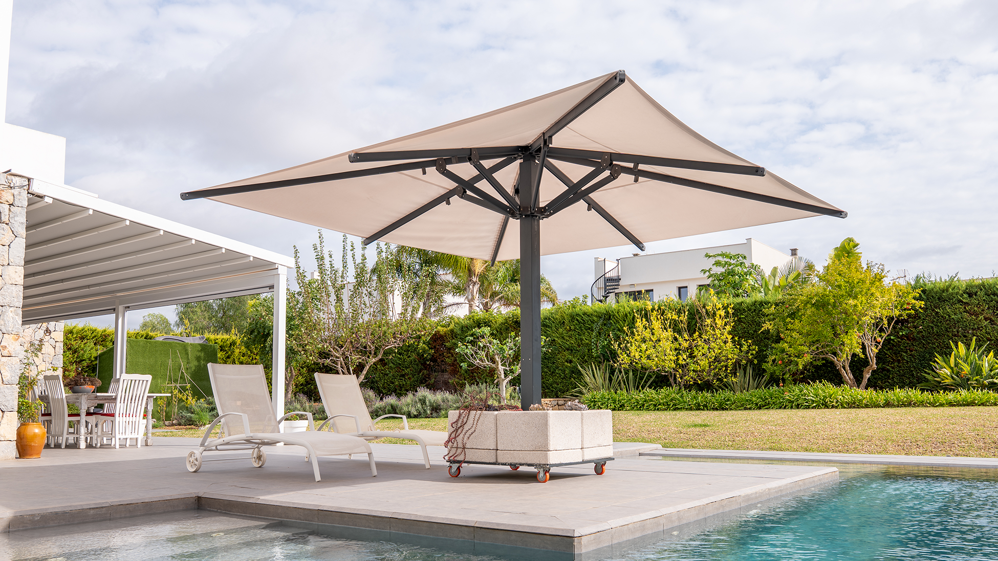 Sombrilla grande beige con estructura metálica junto a dos tumbonas al borde de una piscina.
