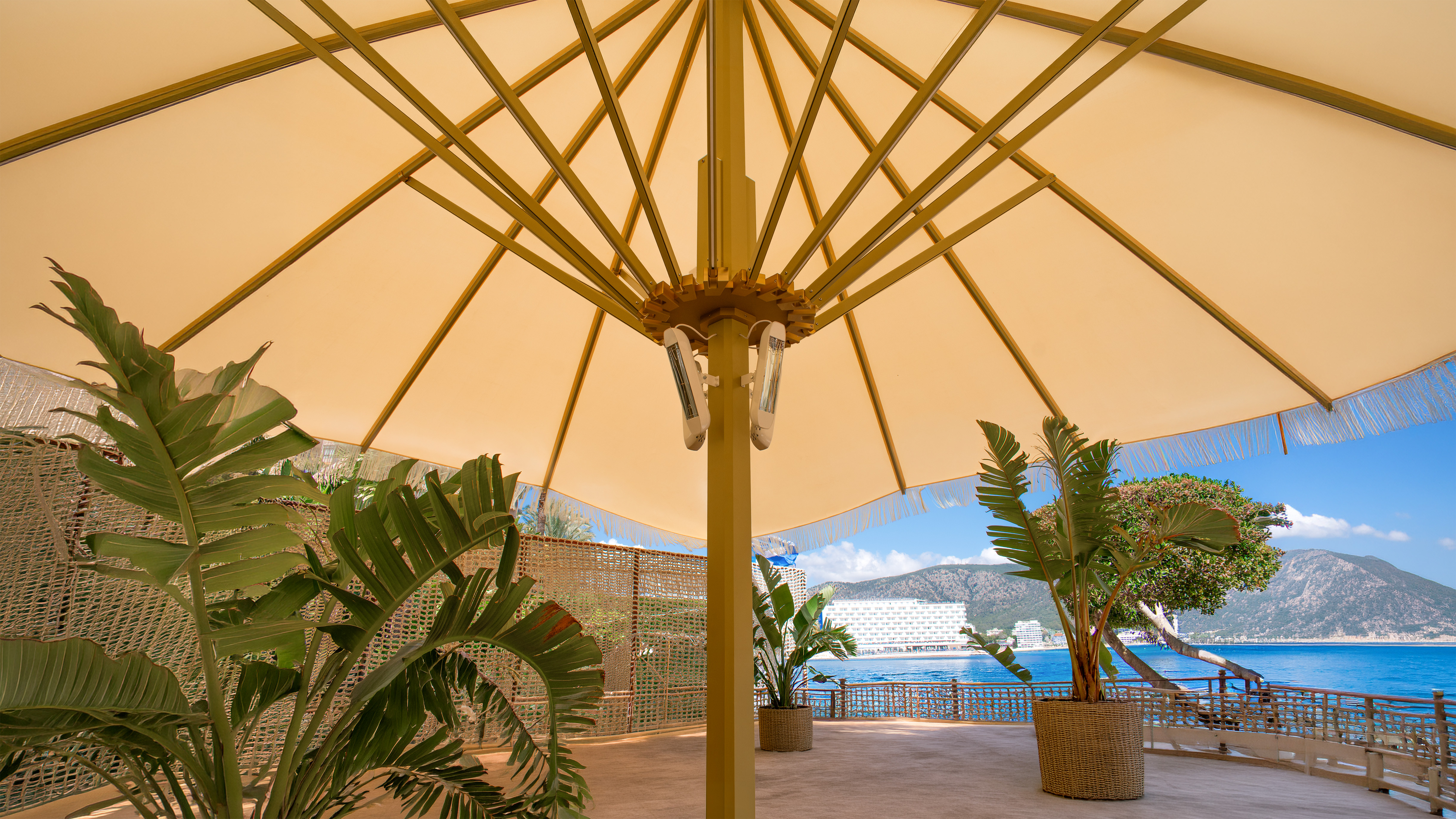 Terraza de restaurante con mesas de madera, sillas grises y un gran parasol negro.