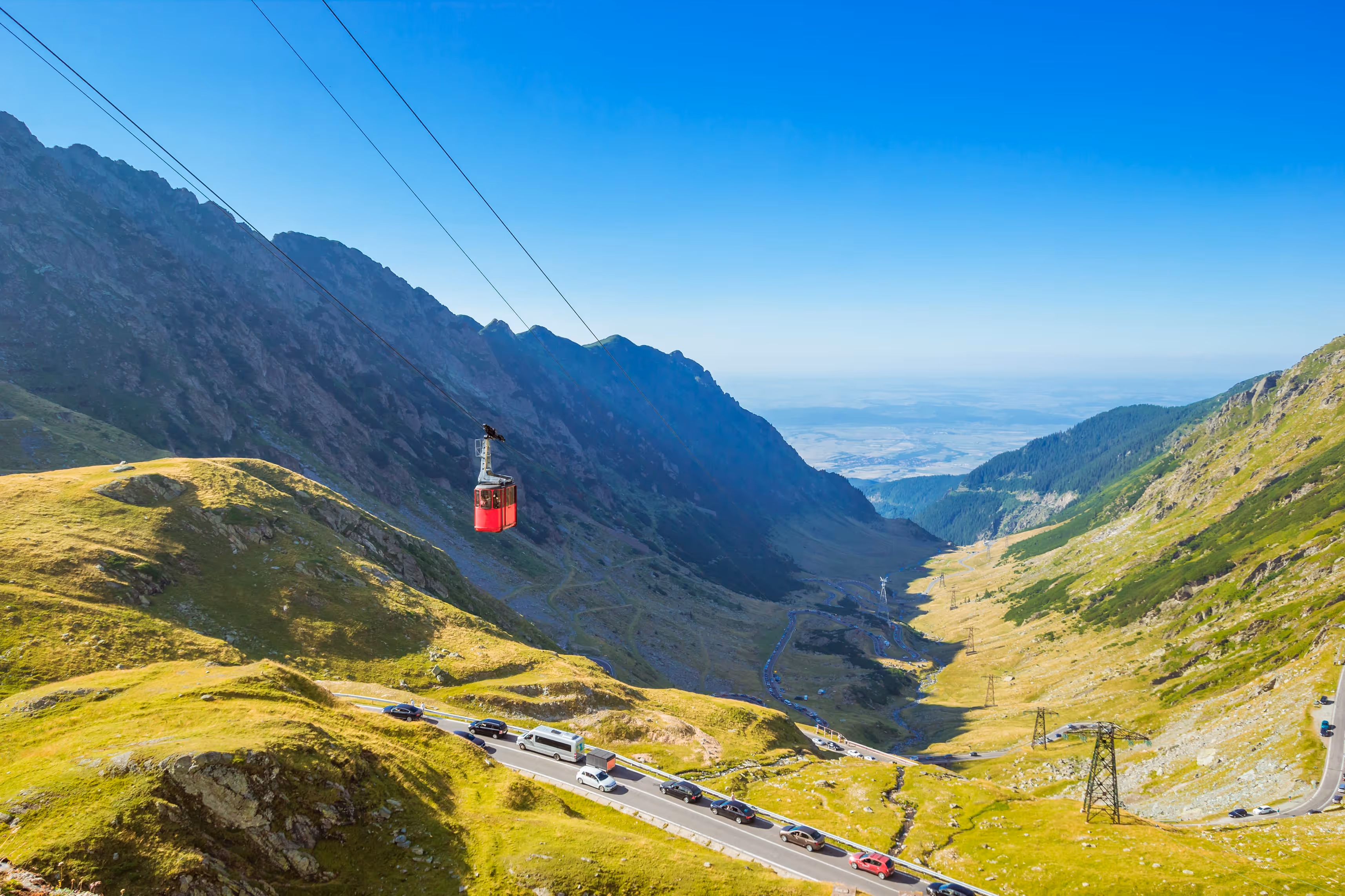 Cabina roșie a telecabinei Bâlea deasupra drumului alpin Transfăgărășan, într-o zi senină