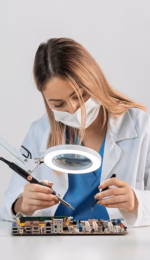 Technician soldering a circuit board under a magnifying lamp