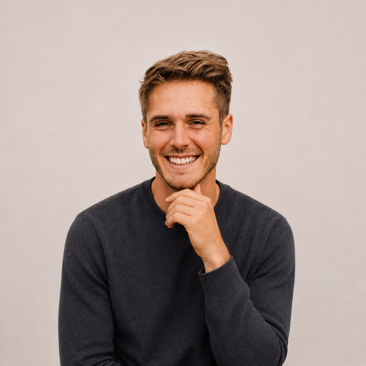 Junger Mann mit braunem Haar und dunklem Pullover lächelt direkt in die Kamera.
