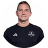 Portrait eines lächelnden Mannes in schwarzem Fußballtrikot vor weißem Hintergrund.