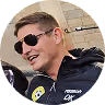 Lächelnder Mann mit Sonnenbrille und blonden Haaren trägt schwarzen Mantel und grünes Mikrofon.
