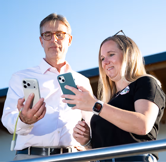 Ein Mann und eine Frau vergleichen zwei Smartphones draußen bei Sonnenlicht.