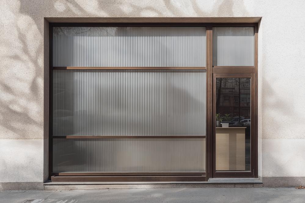 Storefront with frosted glass window and glass door with potted plants inside on a concrete sidewalk.