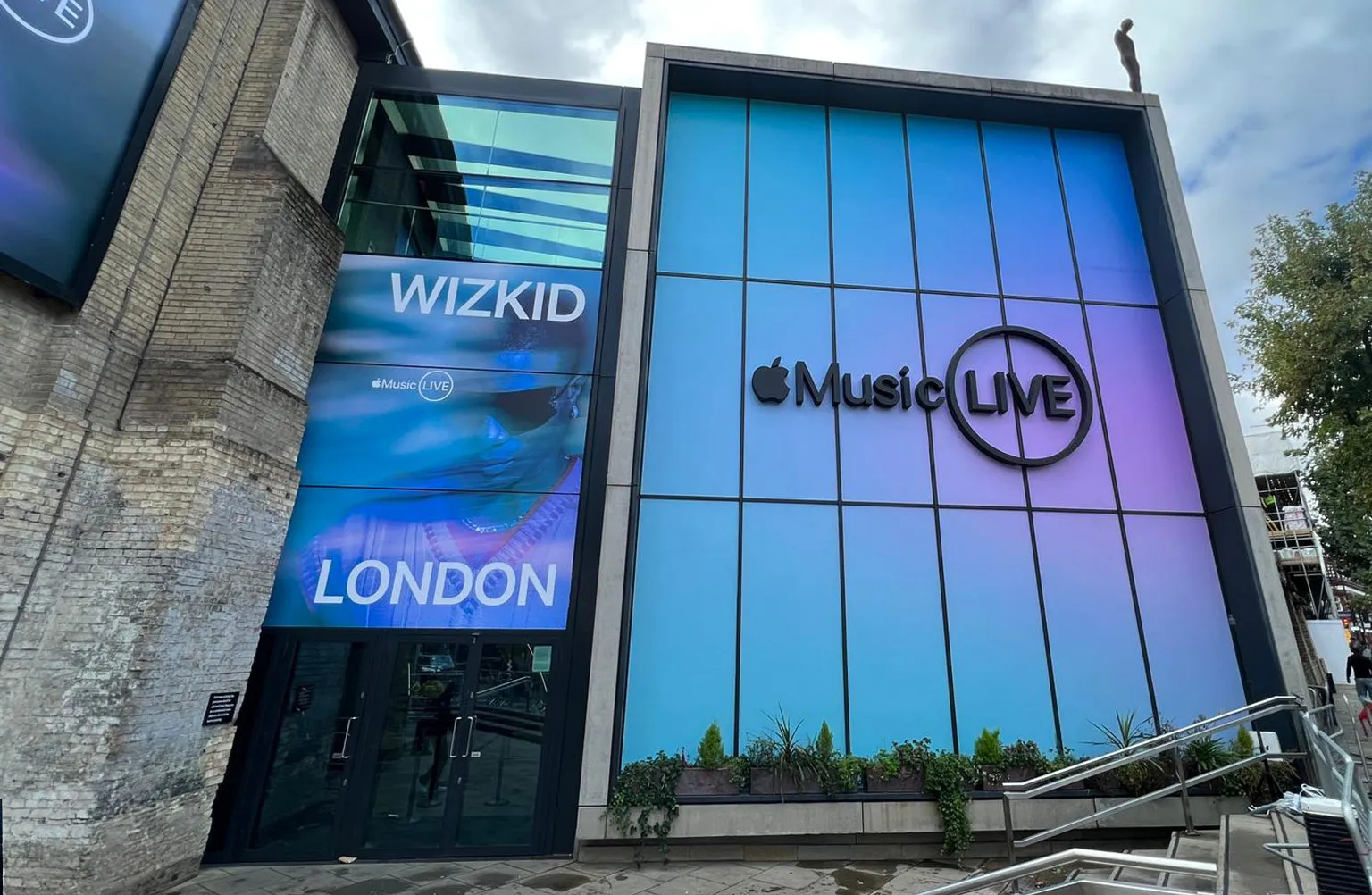 Building with large blue Apple Music Live sign and poster promoting Wizkid London event.