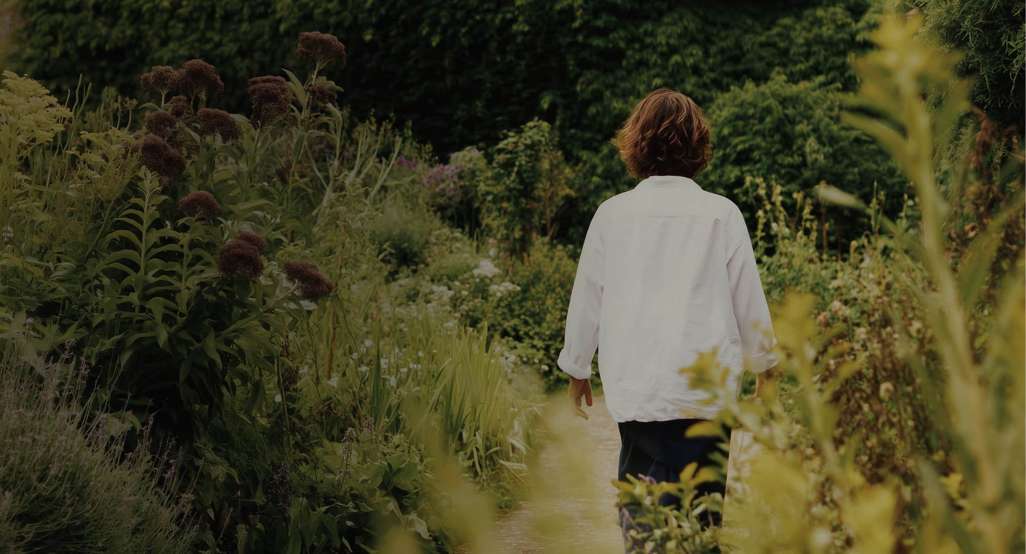 a woman walking on a trail with tall plants