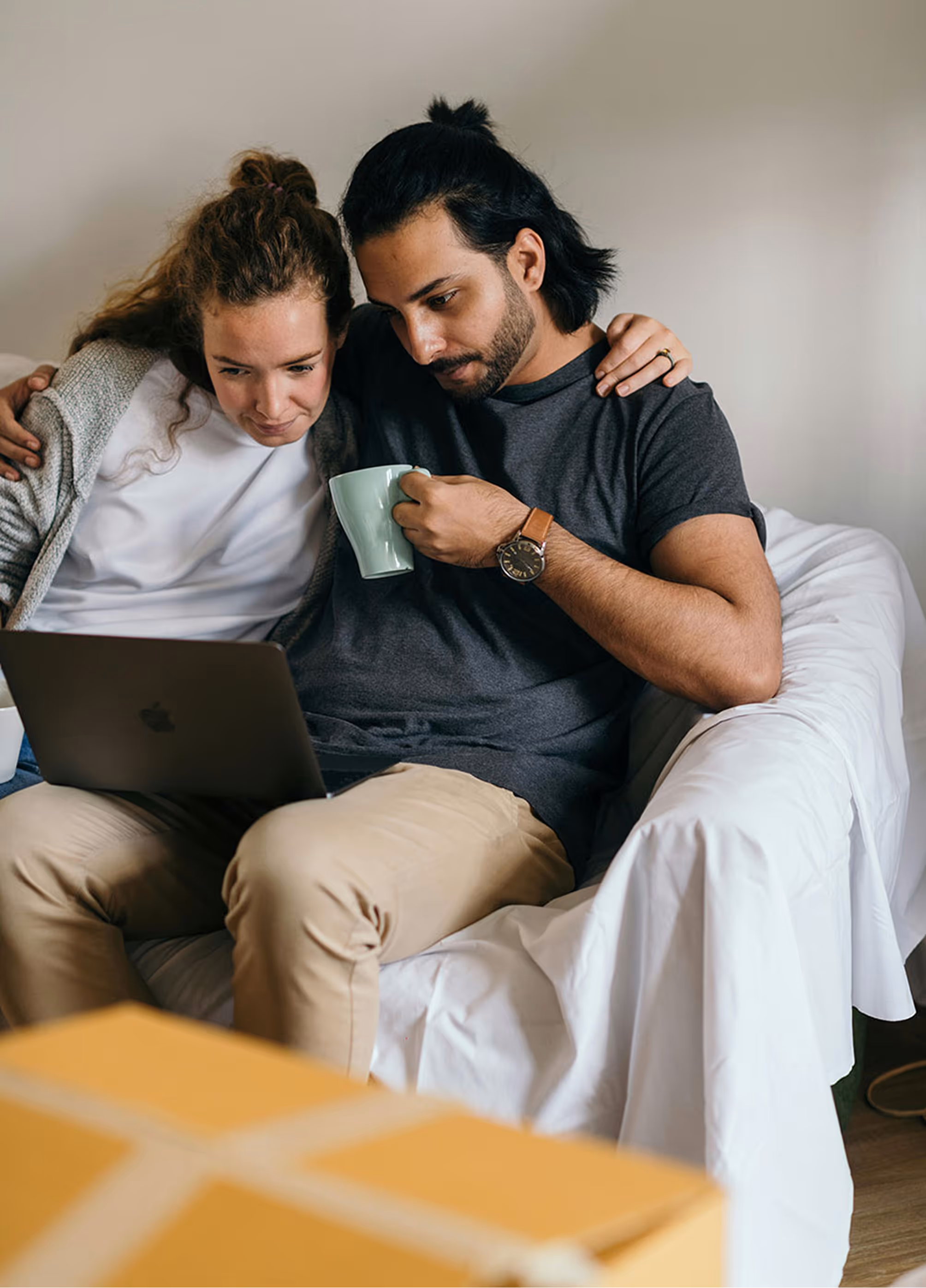 A man and a woman sitting on the couch looking at a laptop