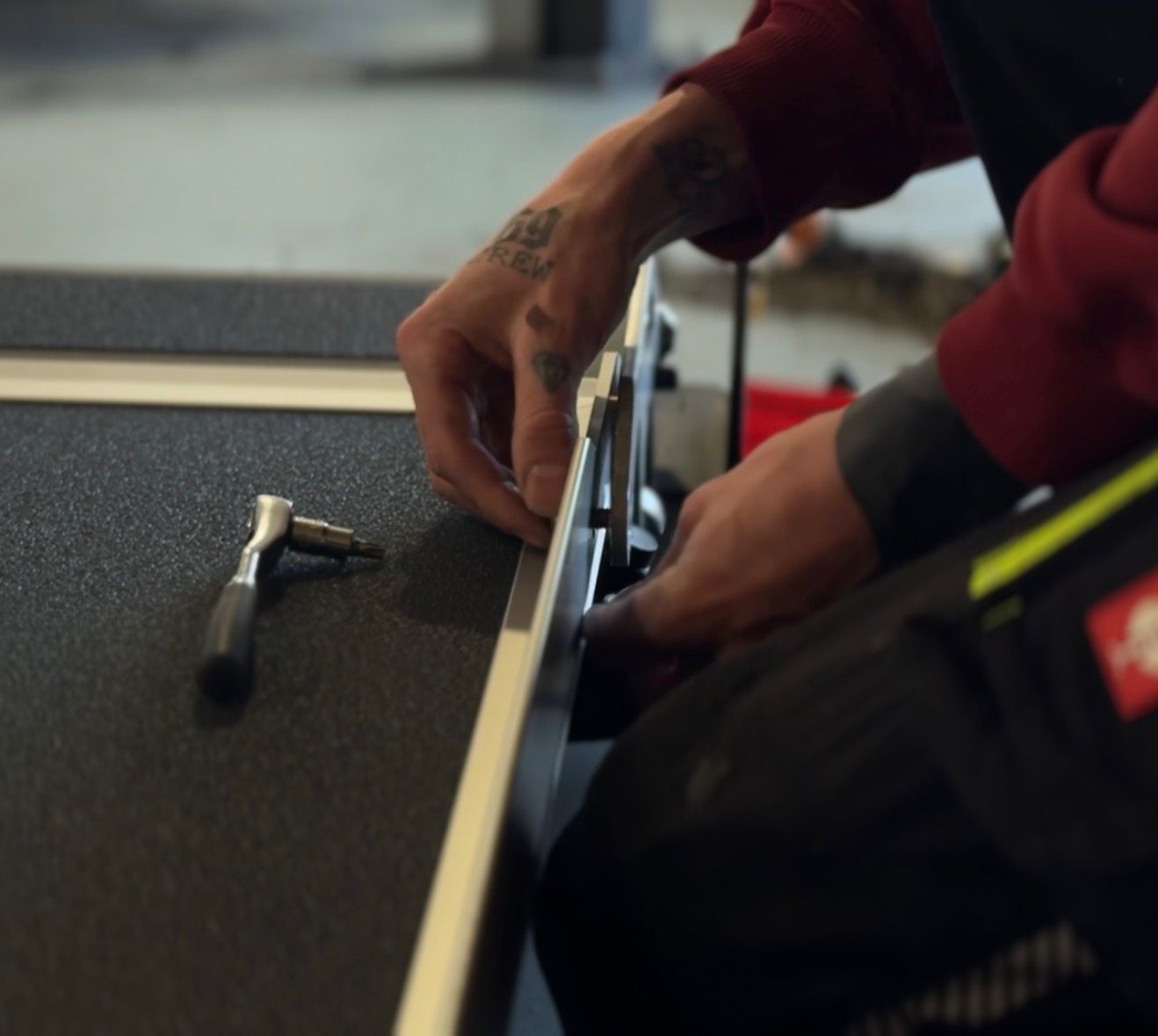 Hands assembling or adjusting a piece of furniture or equipment with a small ratchet tool nearby on a textured surface.
