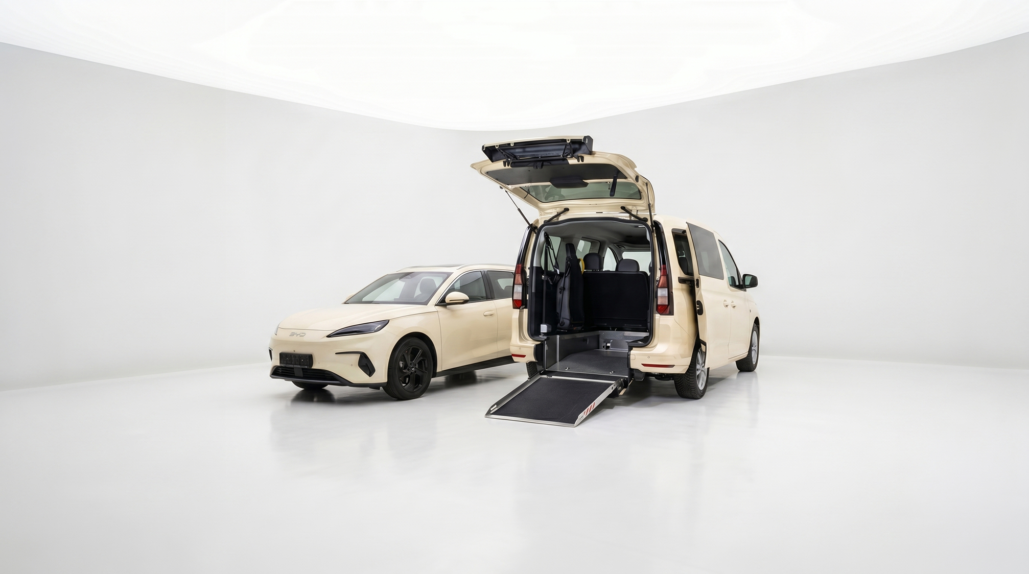 Two cream-colored BYD cars in a white studio, one sedan and one van with an open rear door and extended wheelchair ramp.
