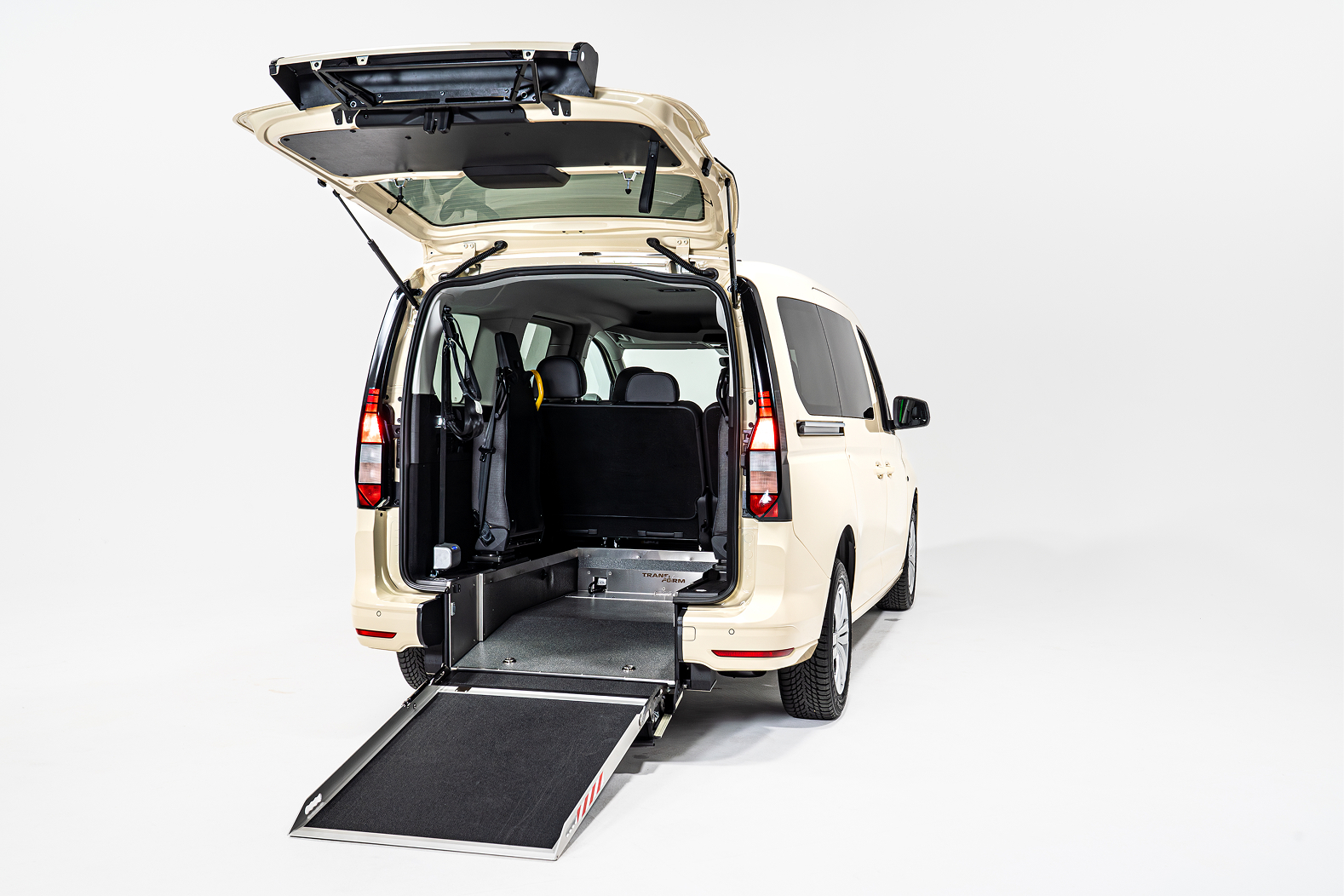 Beige van with rear hatch open and ramp extended for wheelchair access in white studio.