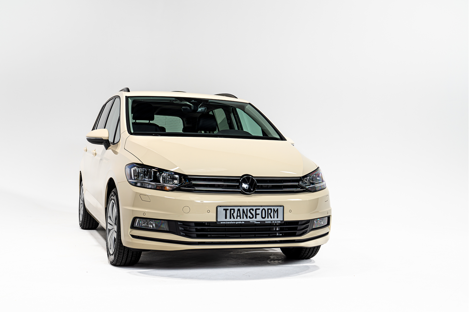Front view of a beige Volkswagen car with TRANSFORM license plate on a white background.