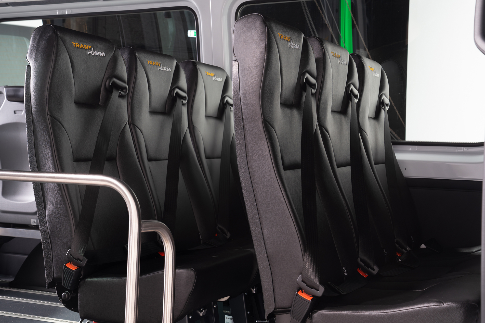 Row of black leather bus seats with seatbelts and TRANSFORM logo on headrests.