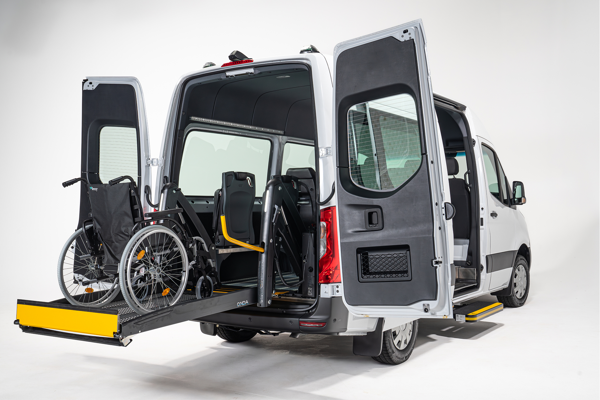 White van with rear doors open, showing a wheelchair on a lift inside the vehicle.