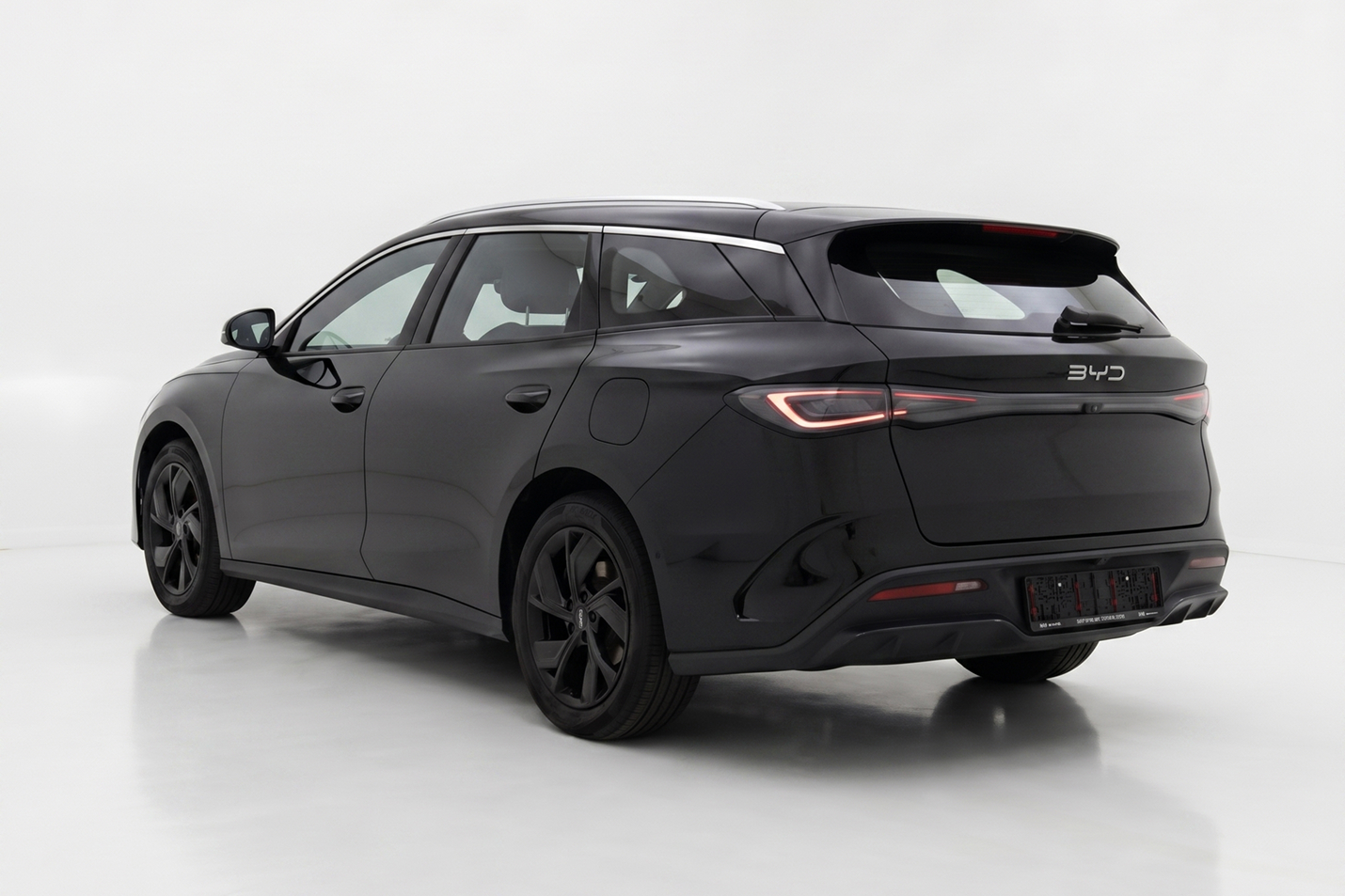 Black BYD electric station wagon with sleek modern design and illuminated rear lights, shown from rear side.