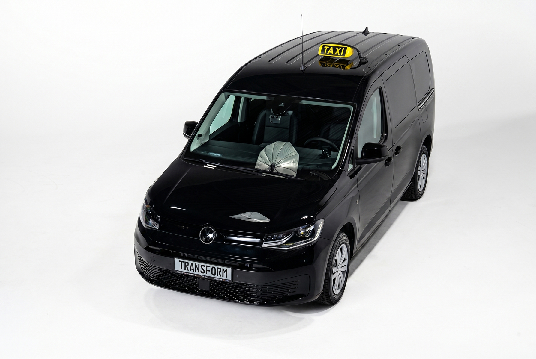 Black van with a yellow taxi sign on top and a license plate reading TRANSFORM on white background.