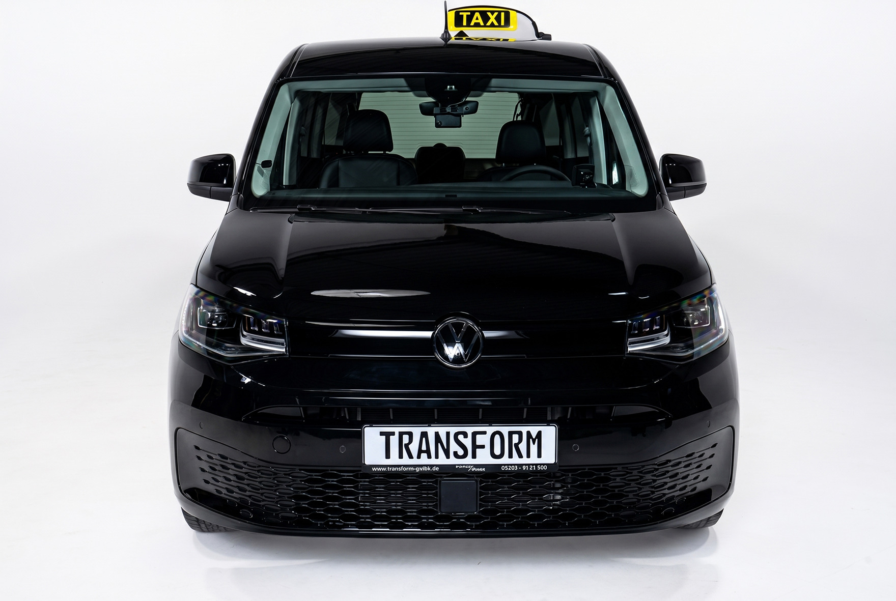 Front view of a black Volkswagen taxi with a 'TRANSFORM' license plate and rooftop taxi sign.