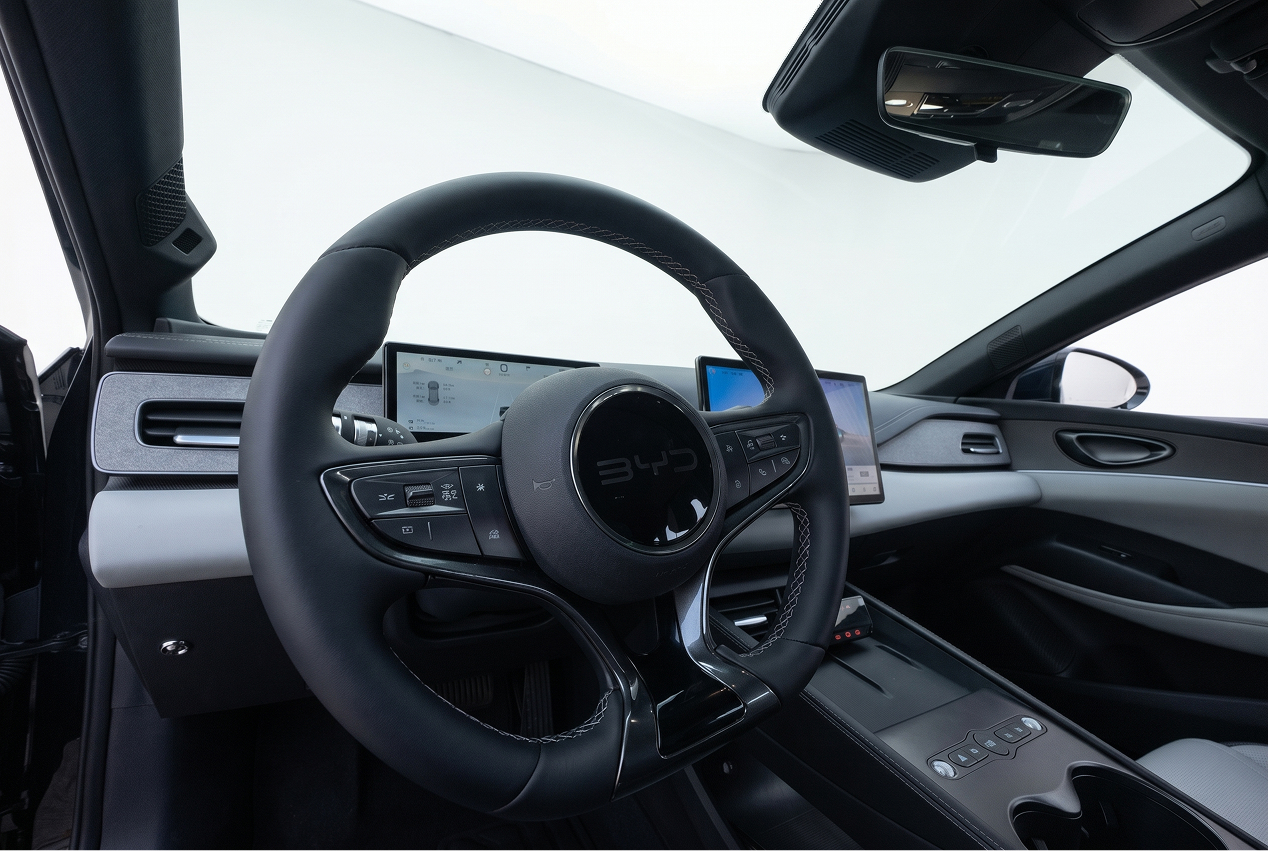 Interior of a modern car showing a black steering wheel with controls and dual digital display screens.