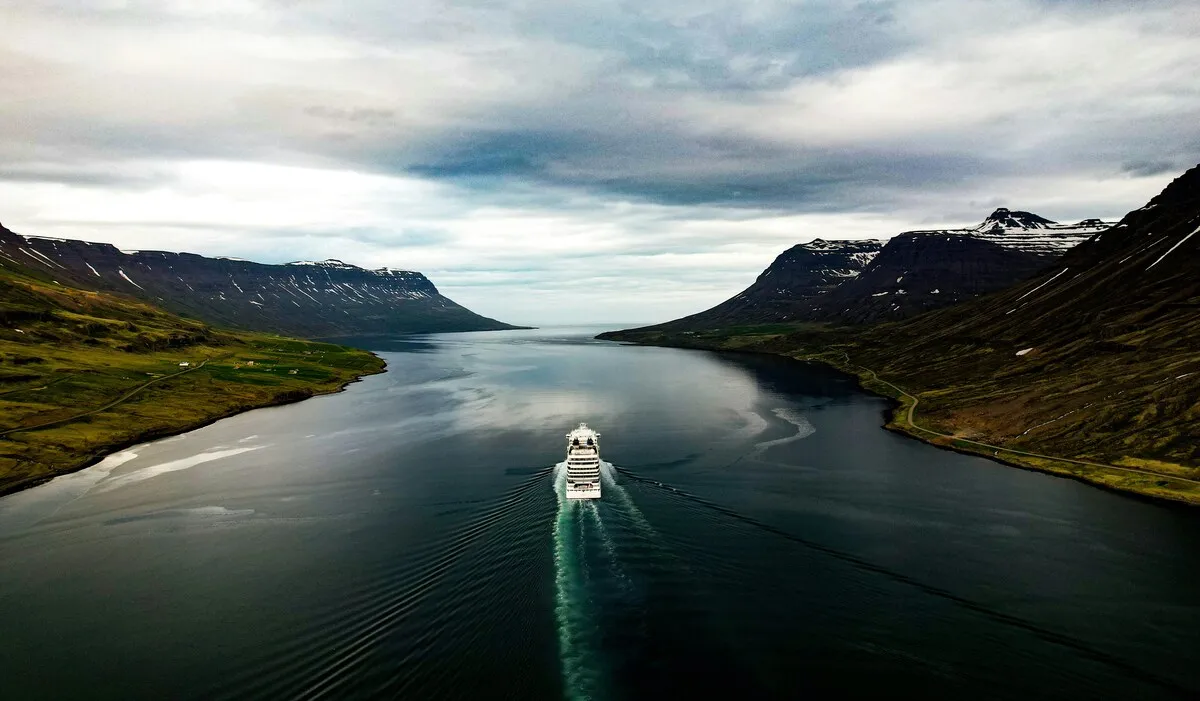 Ship sailing through a wide fjord between snow-capped mountains