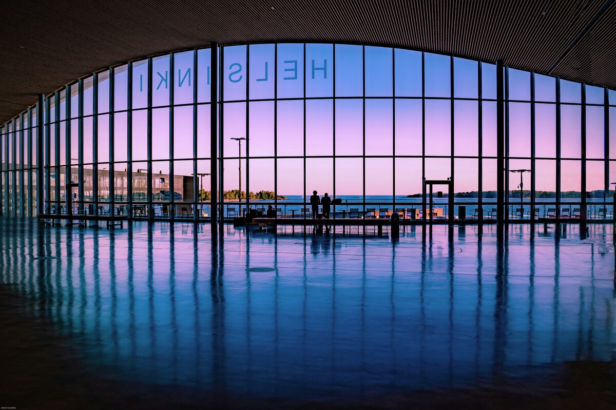 Silhouetted travellers in a glass terminal with Helsinki lettering at dusk