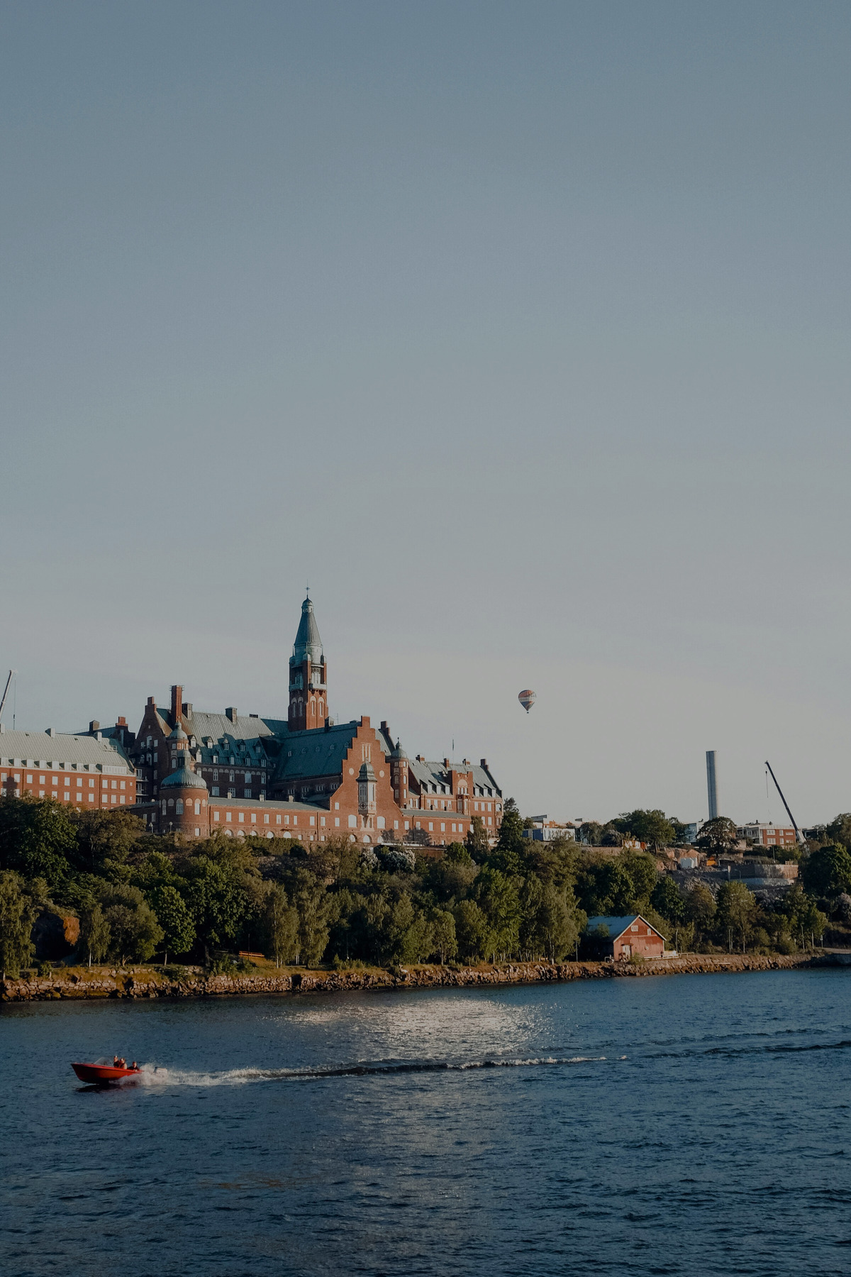 Red-brick waterfront building in Stockholm with a passing speedboat