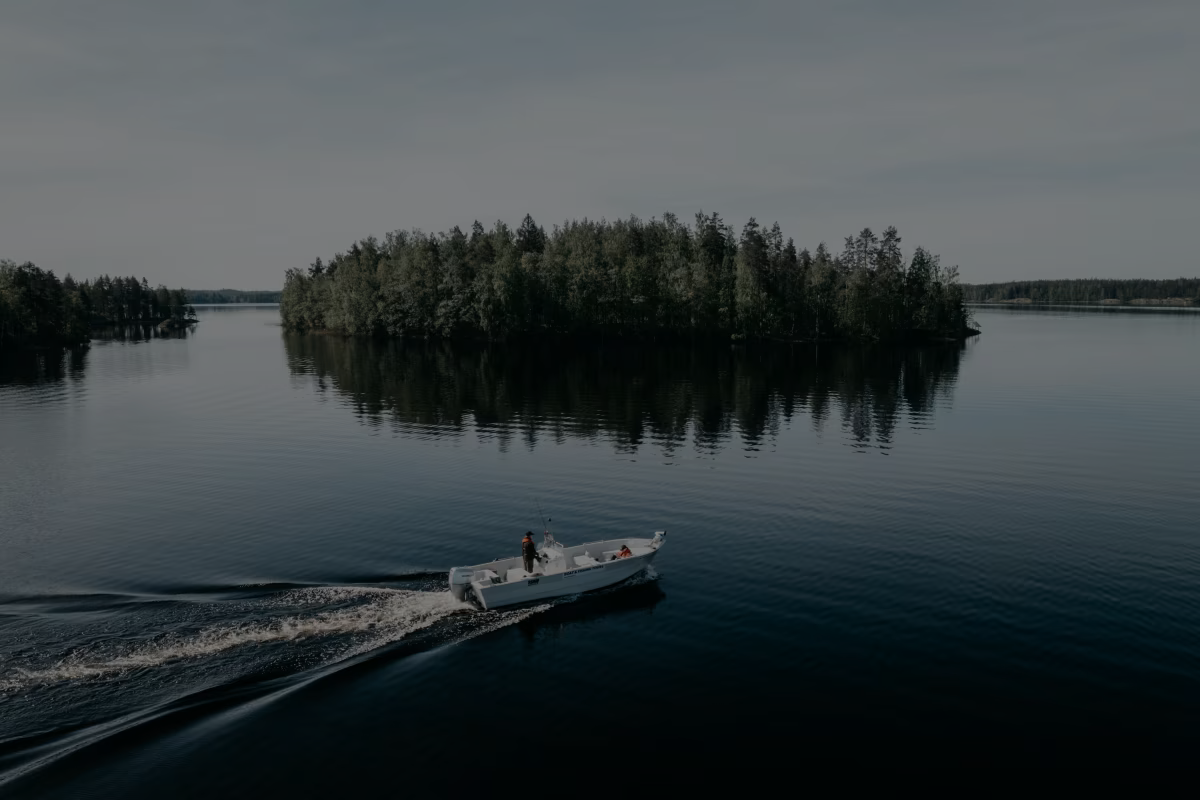 Motorboat crossing a calm Finnish lake past a wooded island