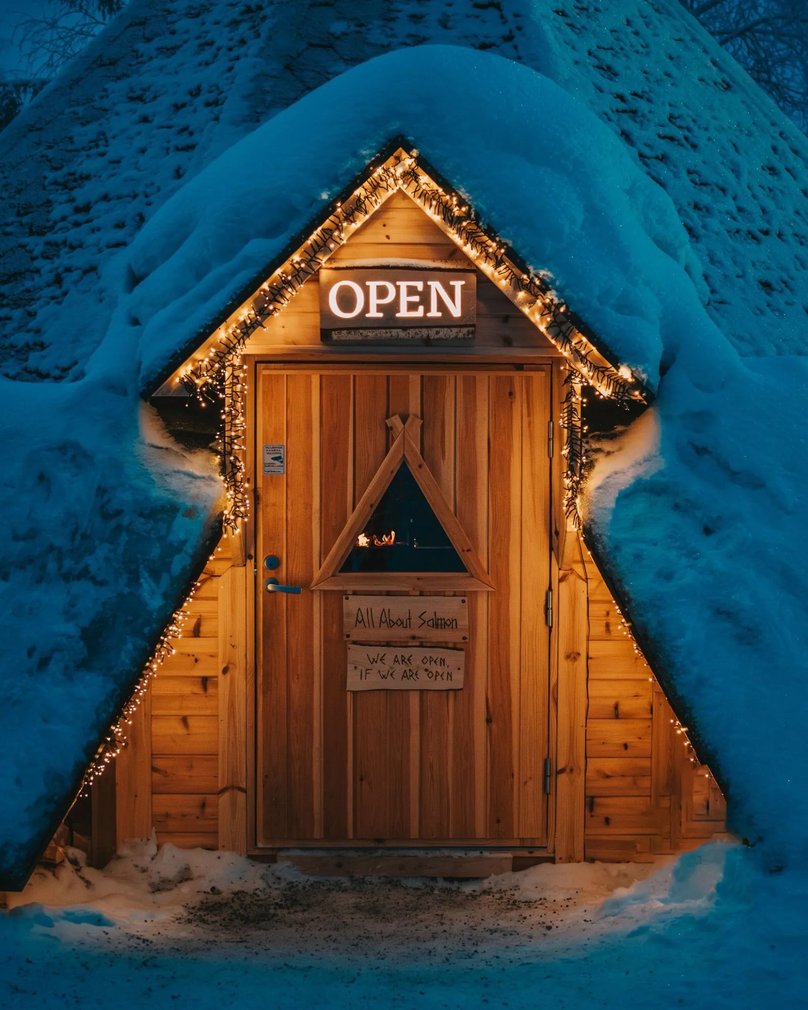 Lit wooden door with an Open sign in a snow-covered hut