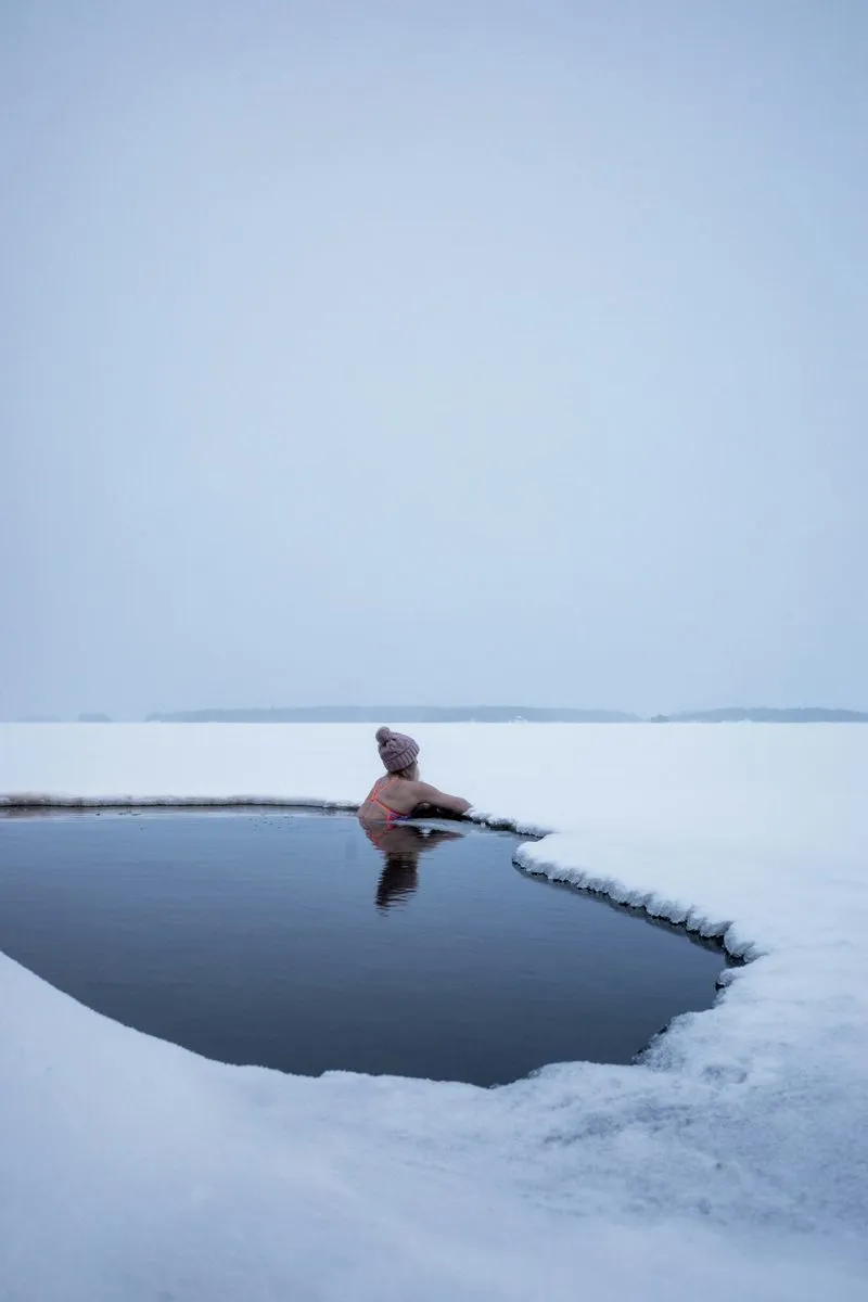 Ice swimmer in an open water hole surrounded by snow in Finnish Lapland