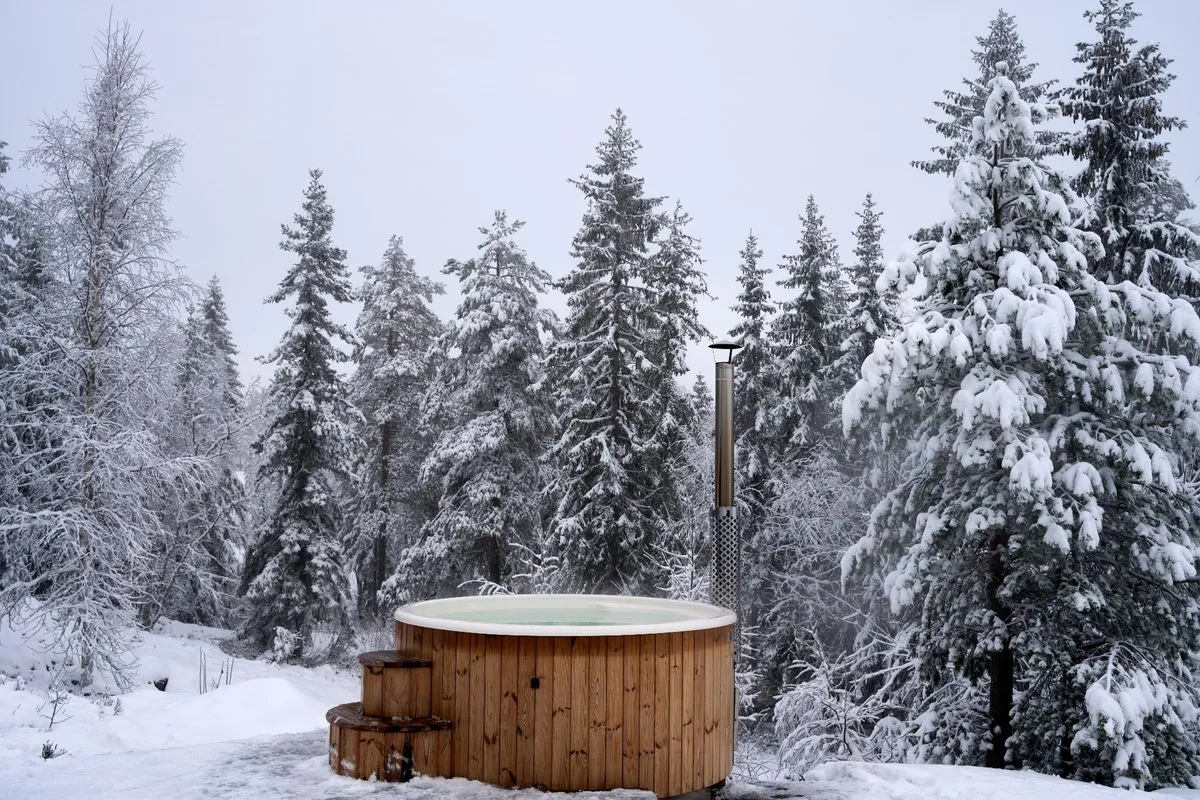 Outdoor wooden hot tub beside a snow-covered forest in Finnish Lapland
