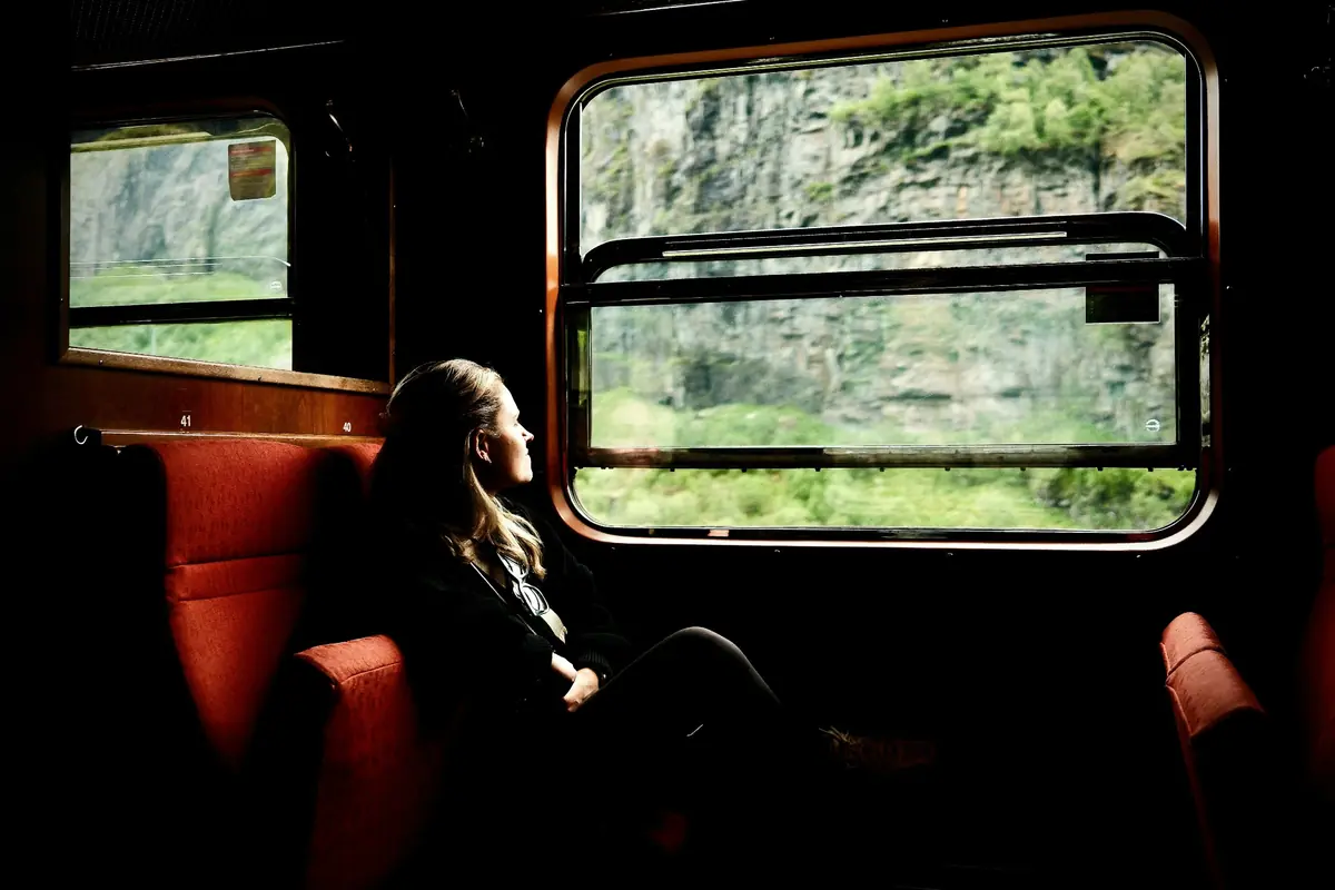 Traveller gazing out of a vintage train window at mossy cliffs