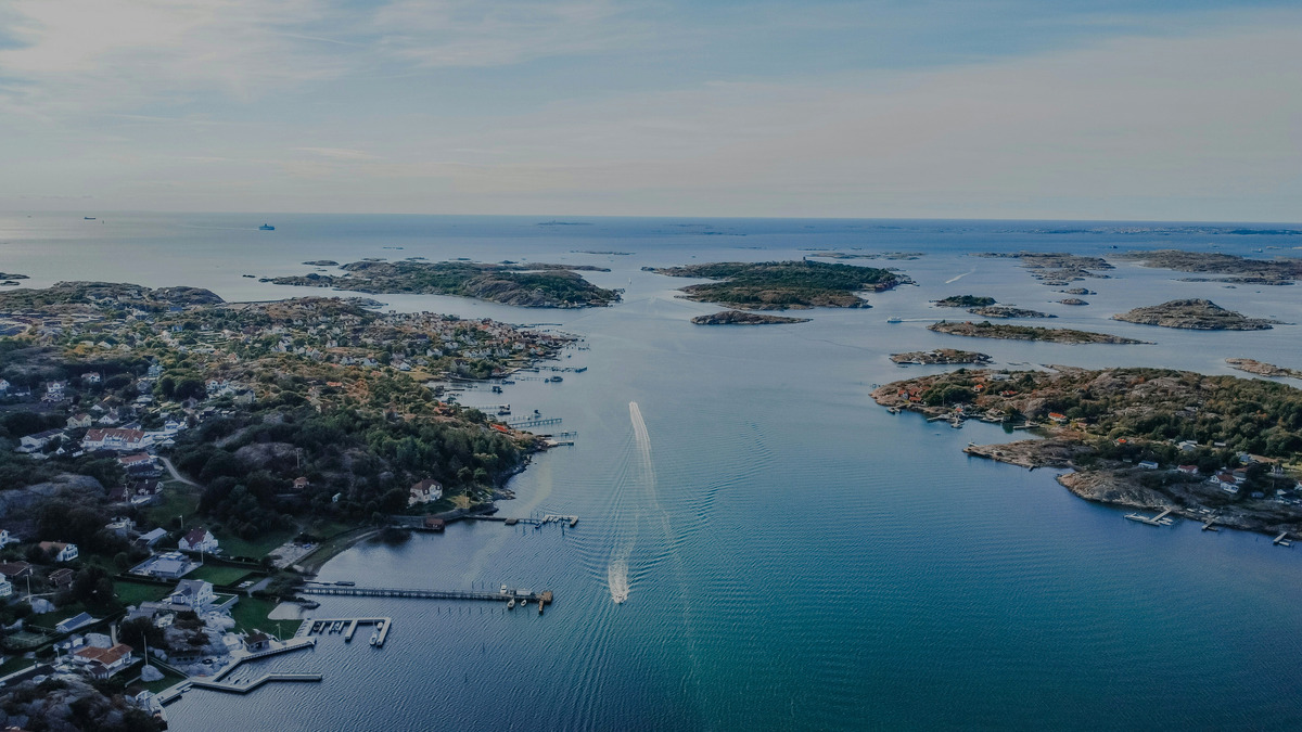 Aerial view of a rocky archipelago with a small harbour and a boat wake on calm water