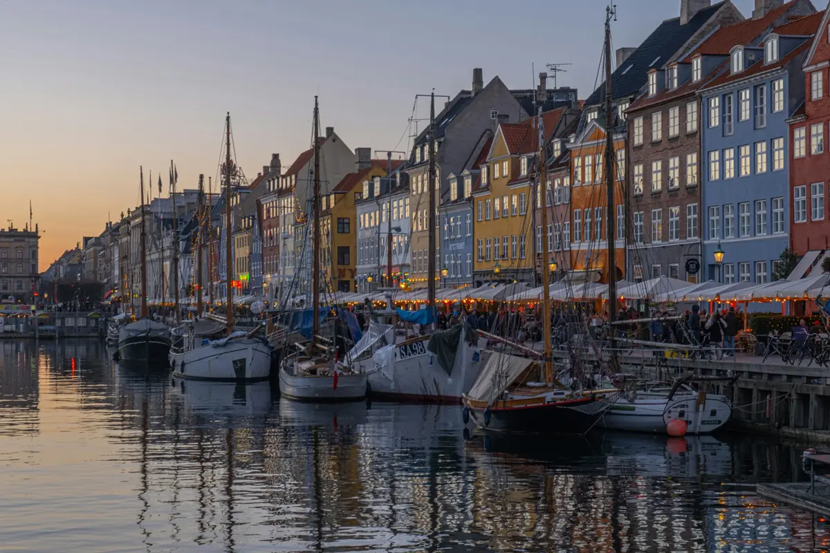 Colourful townhouses and sailing boats along the Nyhavn canal in Copenhagen at dusk
