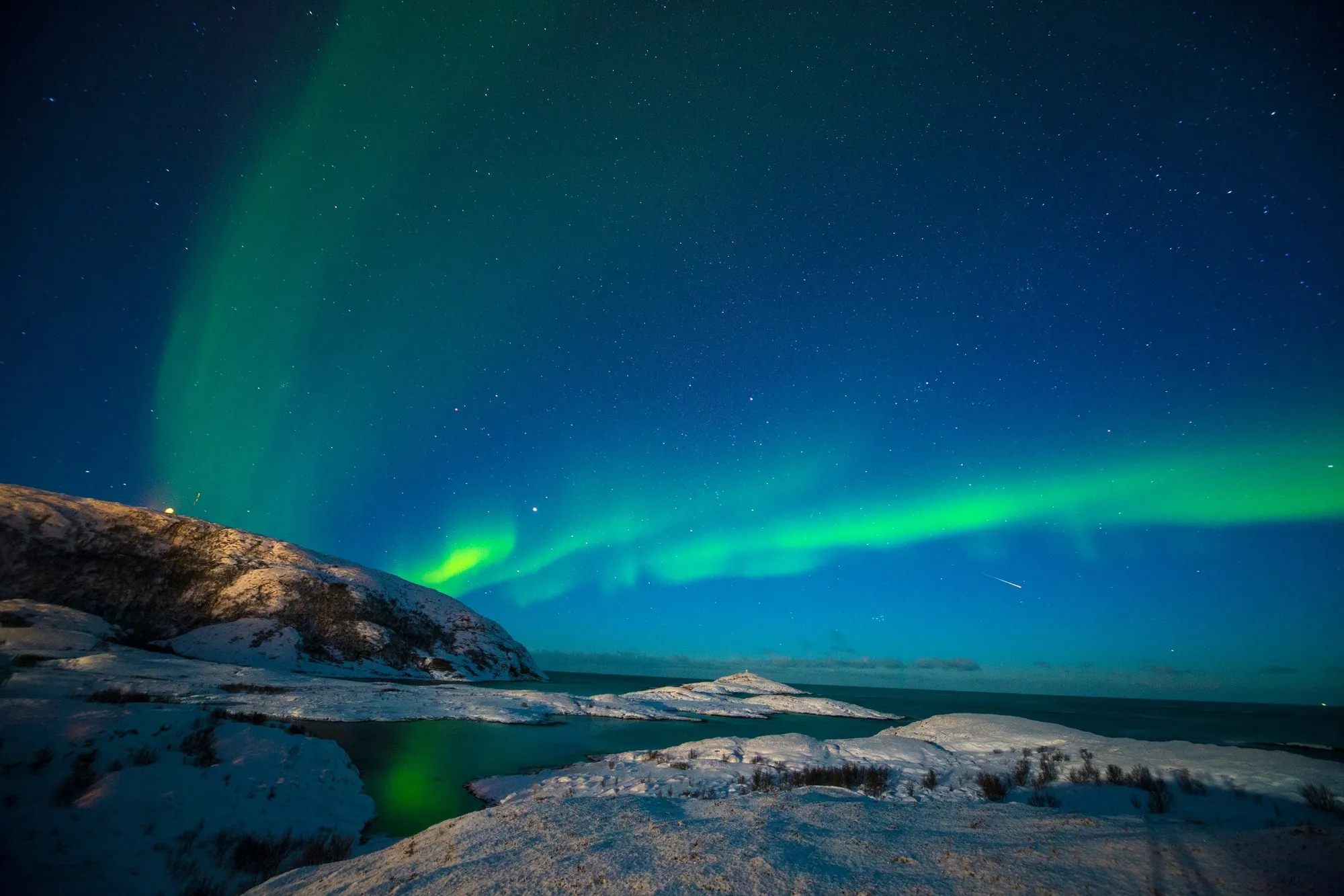Northern Lights glowing green over a snowy Arctic coastline near Tromsø
