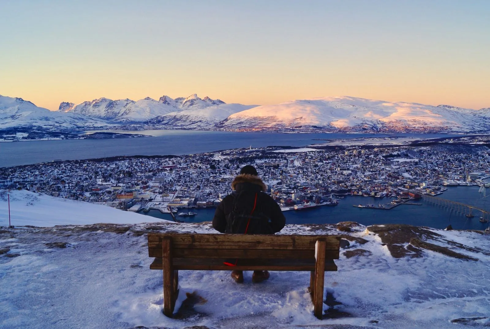 Traveller sitting on a bench above Tromsø, looking out over the city and the snow-covered mountains