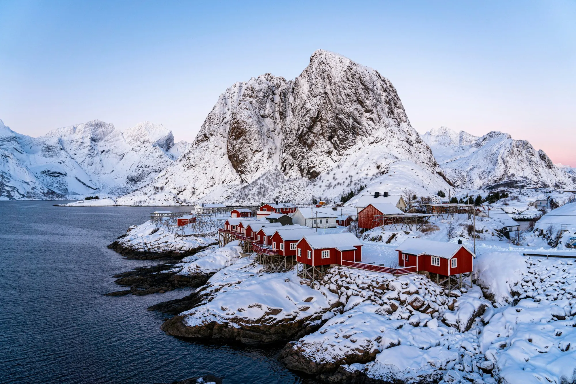 Red fishing cabins beneath snow-covered mountains in a Lofoten village in winter