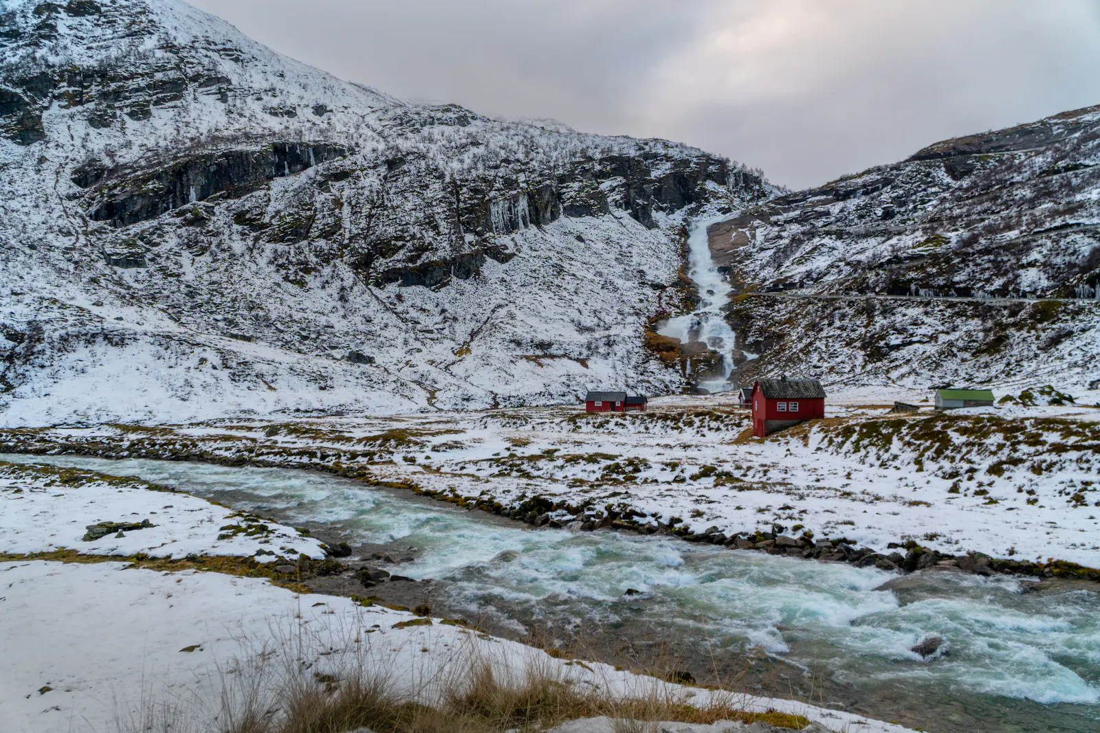Sendefossen waterfall and red wooden cabins in a snowy valley in Vossestrand, western Norway