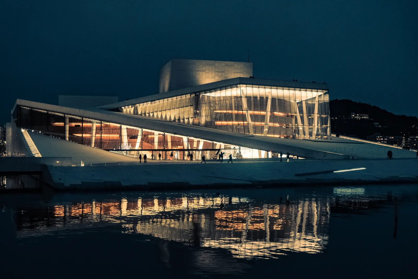 The Oslo Opera House lit up at night and reflected in the water of Bjørvika