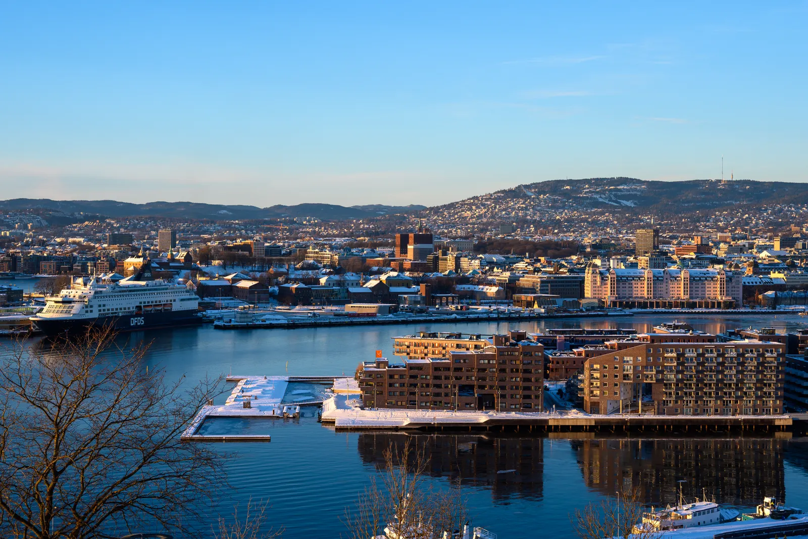 Oslo harbour and city centre under a clear winter sky, with snow on the rooftops