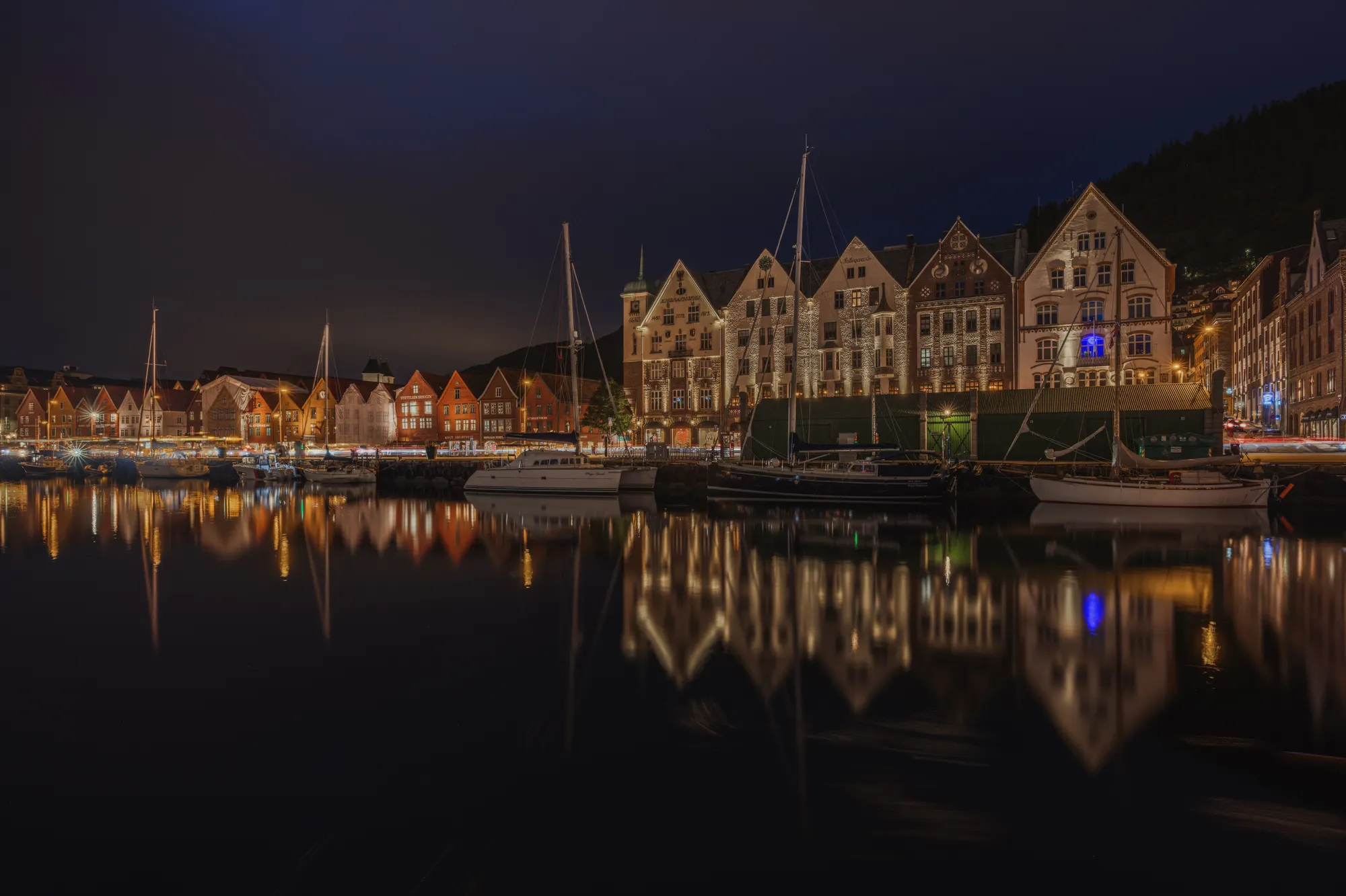 Lit wooden houses of Bryggen reflected in Bergen harbour at night, Bergen, Norway