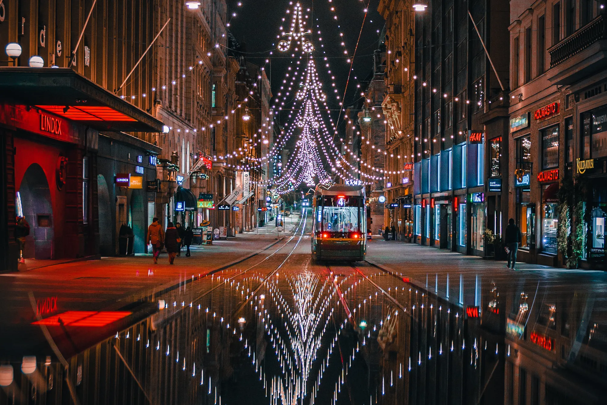 Christmas lights forming a tree above Aleksanterinkatu in central Helsinki at night, reflected on the wet street