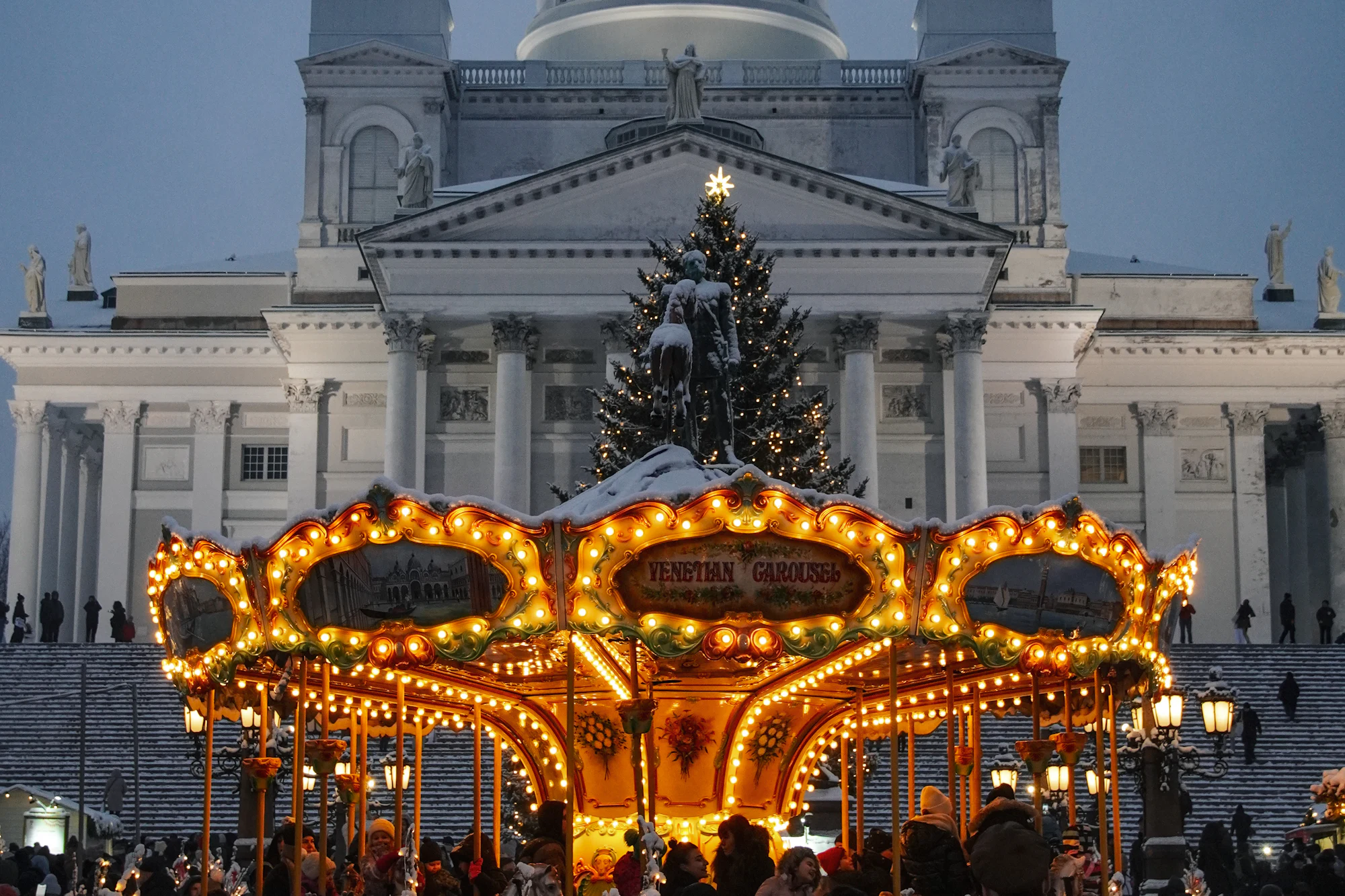 Lit Venetian carousel at the Helsinki Christmas Market in front of Helsinki Cathedral on a snowy winter evening