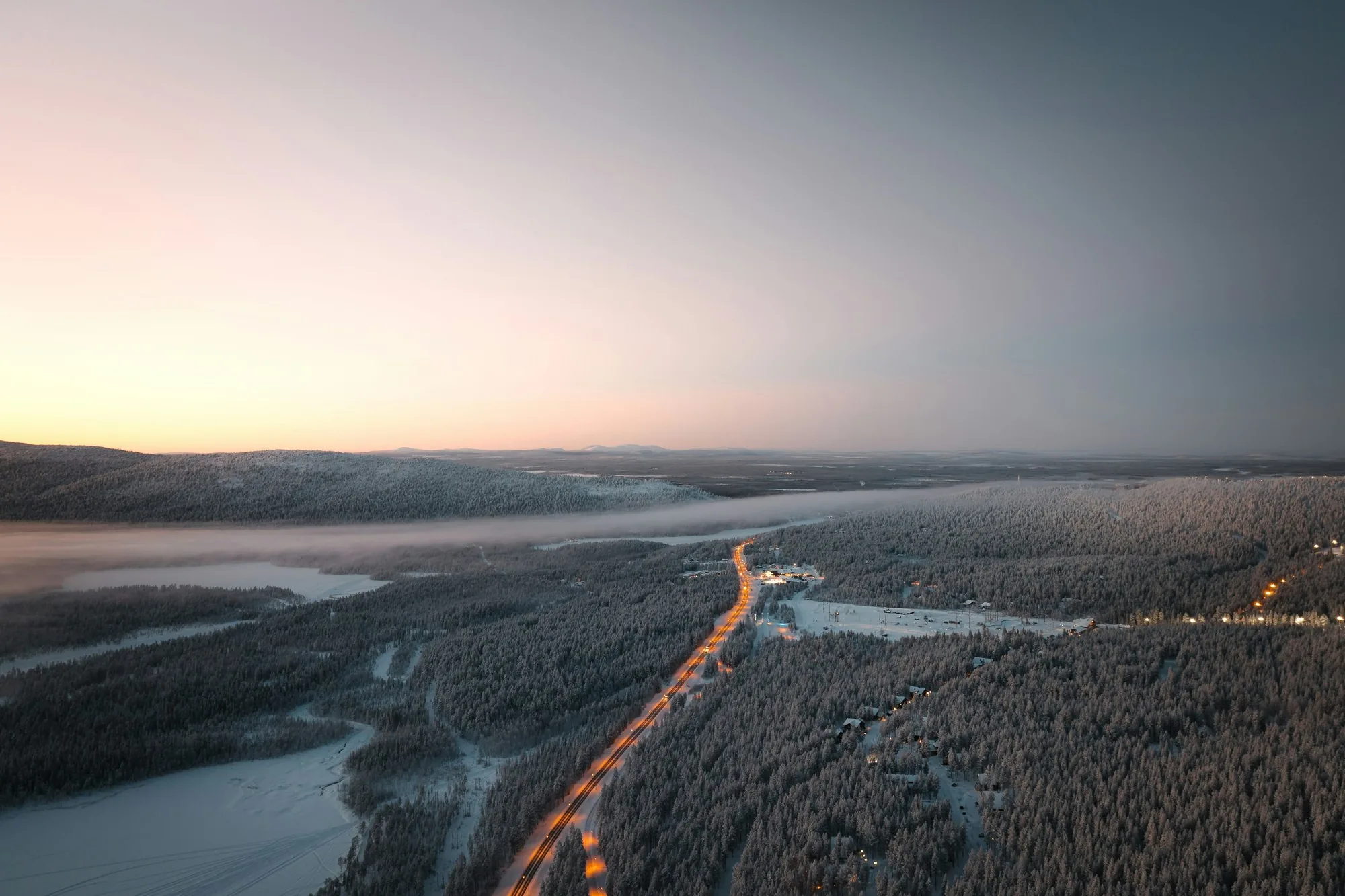 Aerial view of a lit road through snow-covered forest near Levi in Finnish Lapland at winter sunset