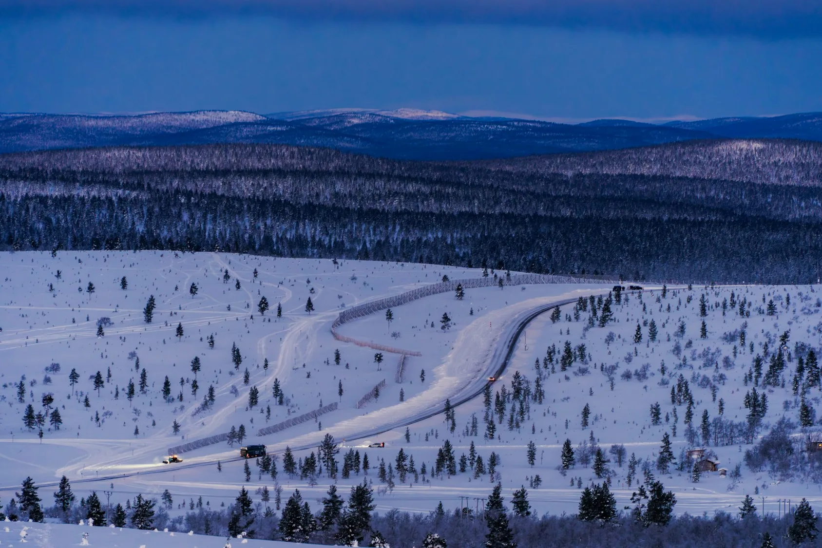 Lit snowmobile trails winding across snowy fells and forest near Saariselkä at dusk