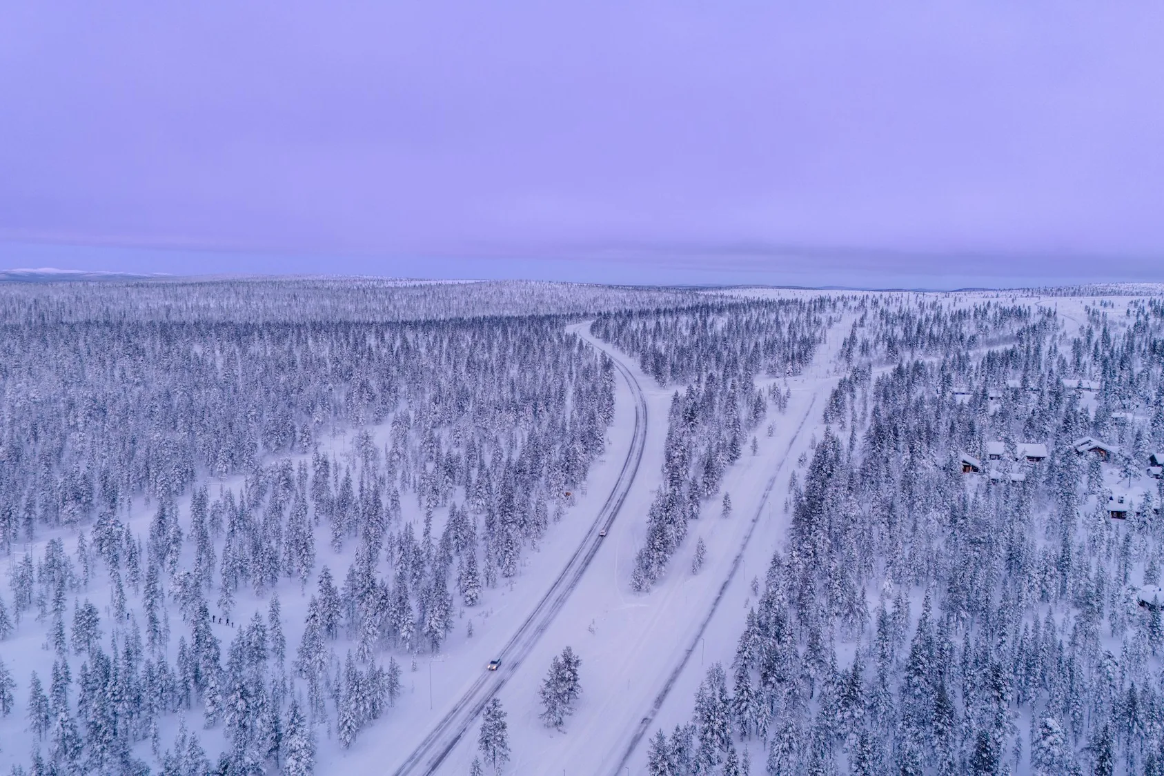 Winter road running through snow-covered forest near Saariselkä in Finnish Lapland at twilight