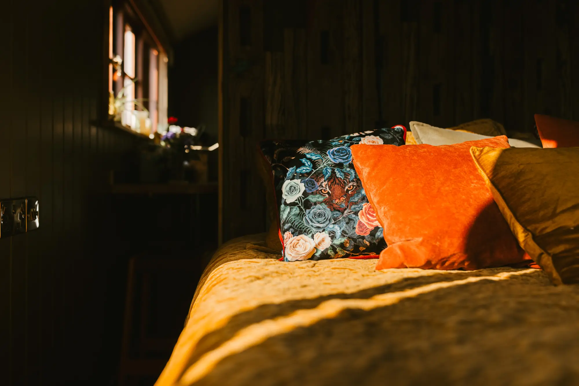 Bed made up with velvet cushions in evening light