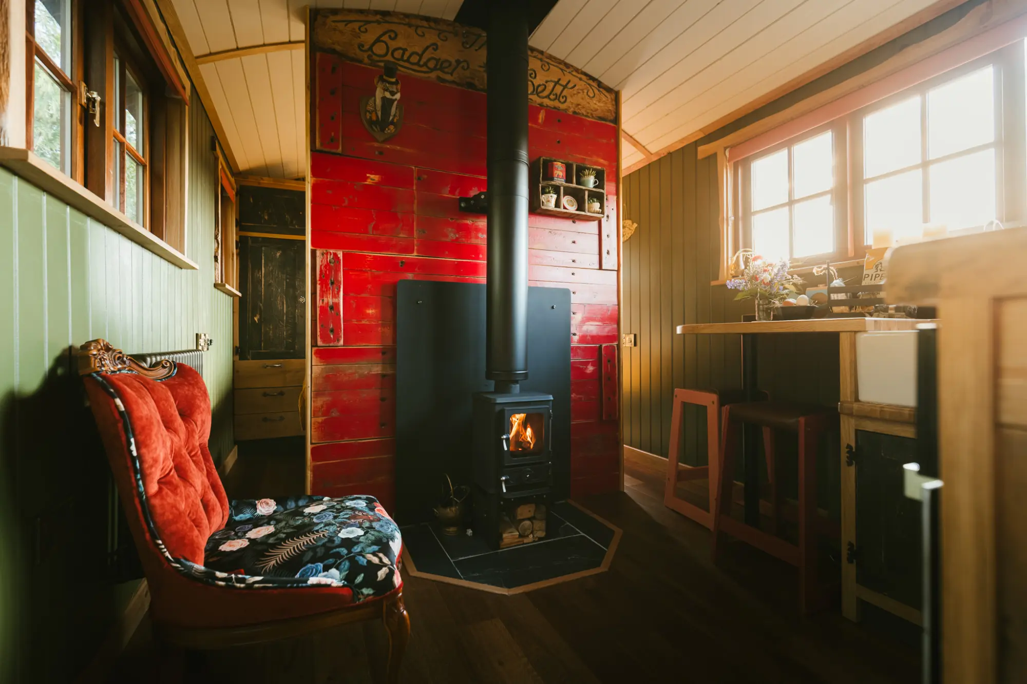 Wood burner alight beside a red velvet chair