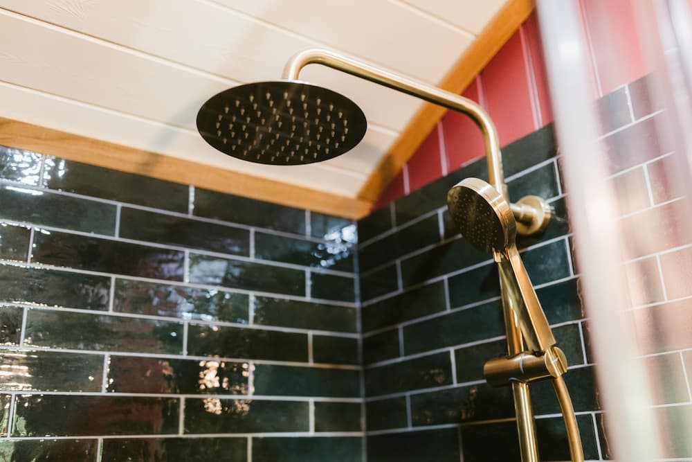 Modern shower with round rainfall and handheld showerheads against dark green tiled walls.