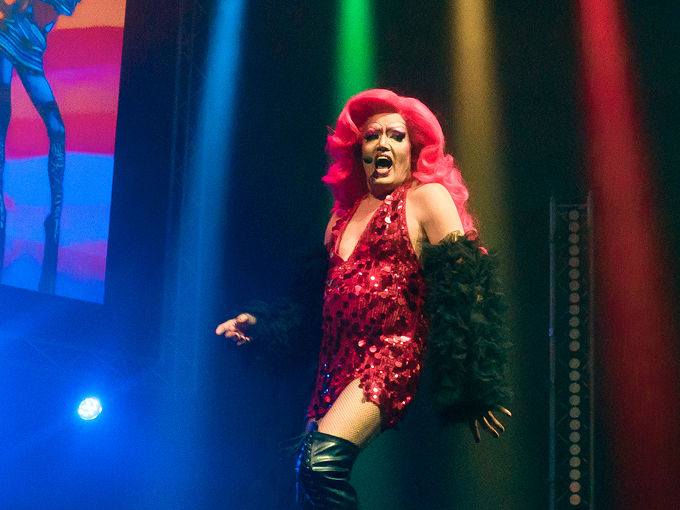 Performer with pink hair on stage under colourful lights
