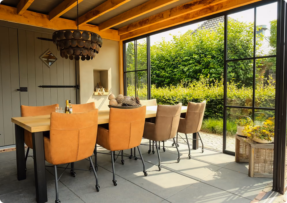 Wooden veranda with modern outdoor sofas and table overlooking a calm river and an orchard at sunset.